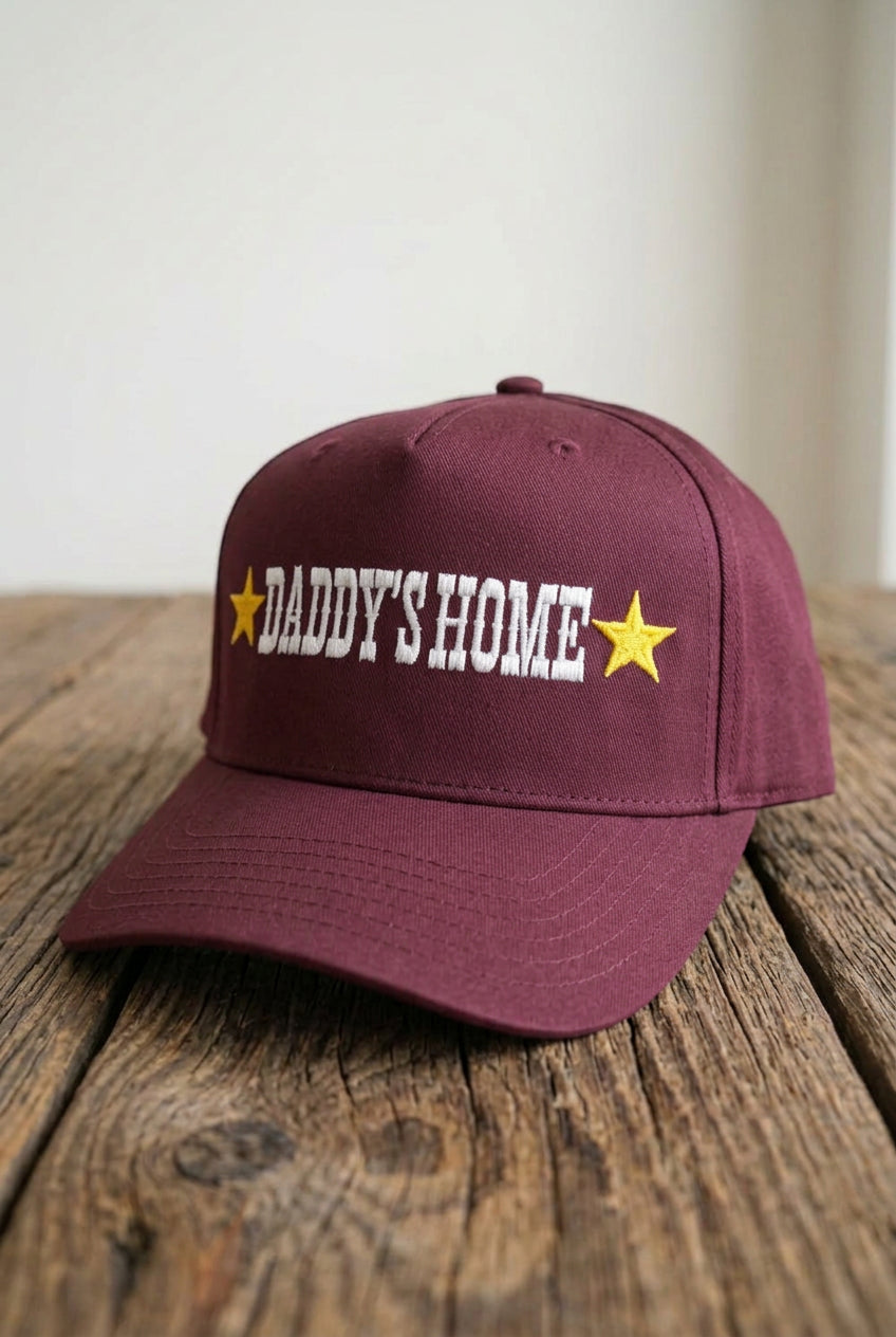 DADDY'S HOME Embroidered Burgundy Trucker, slightly angled front view on a rustic wooden table