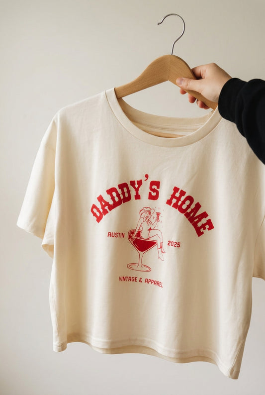 The Cropped Martini Logo Tee hanging on a plain off-white wall