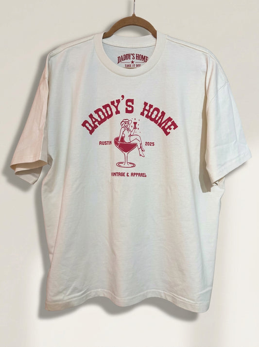 The Oversized Martini Logo Tee hanging on a plain off-white wall